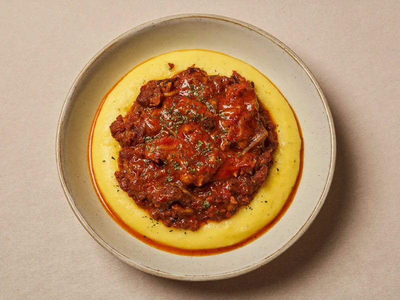 Polenta cremosa con ragù di carne tenero, servita in una ciotola di ceramica
